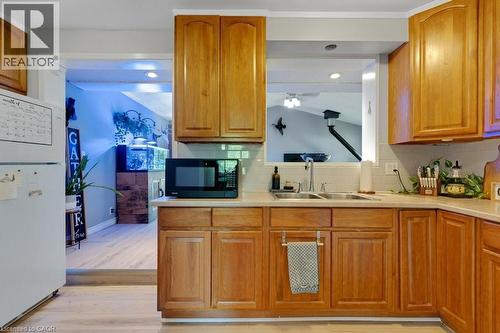 Apartment Kitchen featuring wood cabinetry, light-toned countertops, a stainless steel double-basin sink, and a subway tile backsplash - 3786 Old Beverly Road, North Dumfries, ON 