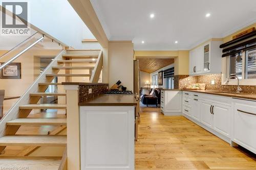 Open-concept kitchen and staircase featuring wood-finish flooring, white cabinetry, a glass and metal railing, recessed lighting, and a multi-toned backsplash - 3786 Old Beverly Road, North Dumfries, ON 