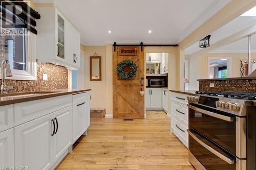 Kitchen featuring wood-finish flooring, white cabinetry with dark hardware, a mosaic tile backsplash, and a stainless steel range - 3786 Old Beverly Road, North Dumfries, ON 