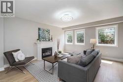 Living area featuring light-toned walls, wood-finish flooring, and a white mantel fireplace with a dark insert - 
