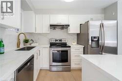 Modern kitchen featuring white cabinetry, stainless steel appliances, light wood-finish flooring, and white countertops with a matching backsplash - 