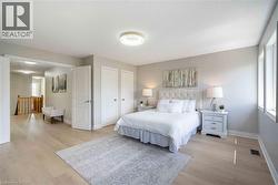 Spacious sleeping area featuring light wood-finish flooring, multiple windows, double entry doors, a built-in ceiling light fixture, and an open doorway to a hallway with wood railings - 