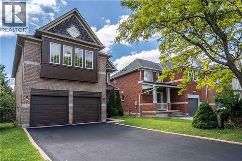 Brick facade residence featuring a two-car garage, asphalt driveway, second-story bay window, and a gabled roofline with shake siding - 2425 Nichols Drive, Oakville, ON - Outdoor