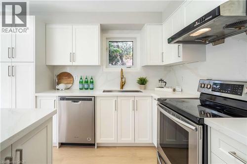 Modern kitchen featuring white shaker cabinetry, stainless steel appliances, a brass-finish faucet, white countertops, and wood-finish flooring - 2425 Nichols Drive, Oakville, ON - Indoor Photo Showing Kitchen With Stainless Steel Kitchen