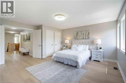 Spacious sleeping area featuring light wood-finish flooring, multiple windows, double entry doors, a built-in ceiling light fixture, and an open doorway to a hallway with wood railings - 2425 Nichols Drive, Oakville, ON - Indoor Photo Showing Bedroom