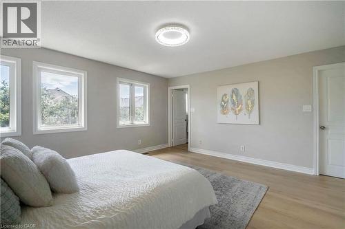 Spacious interior room featuring light wood-finish flooring, multiple windows with white trim, and a contemporary ceiling light fixture - 2425 Nichols Drive, Oakville, ON - Indoor Photo Showing Bedroom