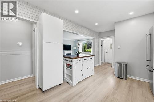 Open-concept kitchen featuring light wood-finish flooring, white brick accent wall, recessed lighting, and a white kitchen island with a wood countertop - 189 Foxbar Road, Burlington, ON 