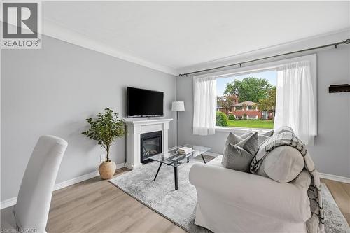 Living area featuring a fireplace with a white mantel, light grey walls, white crown molding, wood-finish flooring, and a large window - 189 Foxbar Road, Burlington, ON 