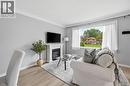 Living area featuring a fireplace with a white mantel, light grey walls, white crown molding, wood-finish flooring, and a large window - 189 Foxbar Road, Burlington, ON 