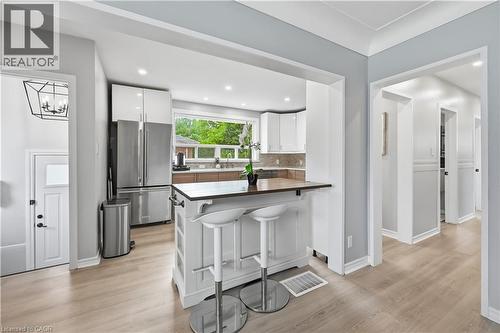Kitchen featuring a breakfast bar with wood-finish countertop, white cabinetry with stainless steel appliances, a multi-pane window, and wood-finish flooring - 189 Foxbar Road, Burlington, ON 