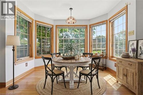 Bay window dining area featuring grid-pattern windows with natural wood trim, wood-finish flooring, a rustic wood sideboard, and a decorative pendant light fixture - 3 Ancaster Street E, Dundas, ON - Indoor Photo Showing Dining Room