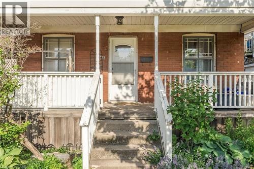 Brick facade featuring a covered porch, white railing, and concrete steps - 295 Keswick Court, Hamilton, ON 