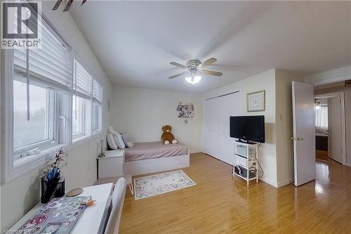 Bright room featuring multiple windows with blinds, wood-finish flooring, a ceiling fan with integrated lighting, and white bi-fold closet doors - 233 Benesfort Crescent, Kitchener, ON 