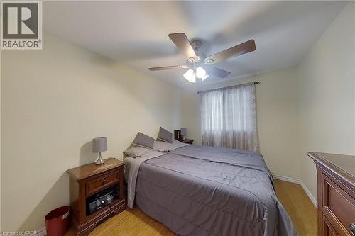 Bedroom featuring wood-finish flooring, a ceiling fan with integrated lighting, and a window with sheer and blackout curtains - 233 Benesfort Crescent, Kitchener, ON 