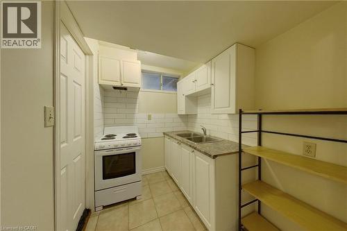 Compact kitchen featuring white cabinetry, a double basin stainless steel sink, a built-in electric range, and light-toned tile flooring - 233 Benesfort Crescent, Kitchener, ON 
