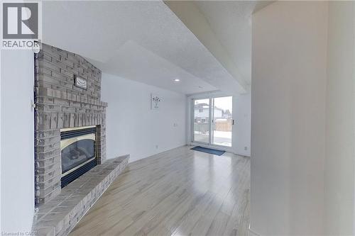 Corner brick fireplace with hearth, wood-finish flooring, recessed lighting, and patio door access - 233 Benesfort Crescent, Kitchener, ON 