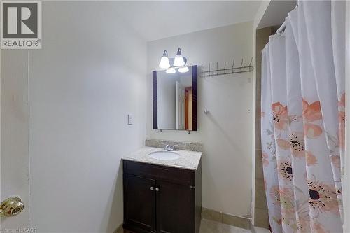 Vanity with a dark wood-finish cabinet and a light-toned stone countertop, featuring an integrated sink and wall-mounted mirror - 233 Benesfort Crescent, Kitchener, ON 