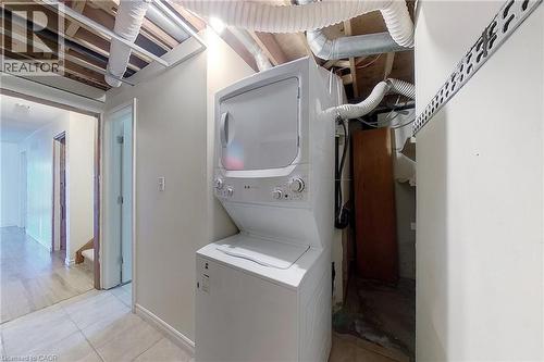 Compact laundry area featuring a stacked washer and dryer, tile flooring, and exposed ceiling joists - 233 Benesfort Crescent, Kitchener, ON 