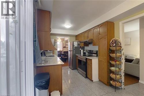 Kitchen featuring wood cabinetry, stainless steel appliances, white countertops, a tile backsplash, and tile flooring - 233 Benesfort Crescent, Kitchener, ON 