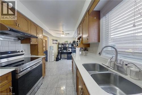 Kitchen featuring wood-finish cabinetry, white countertops, a stainless steel double-basin sink with a pull-down faucet, a stainless steel range, and tile flooring - 233 Benesfort Crescent, Kitchener, ON 