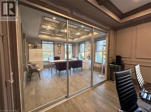 Interior room featuring glass sliding doors, wood-finish flooring, a coffered ceiling, and paneled wall details - 385 E Wilson Street E Unit# 201, Ancaster, ON 