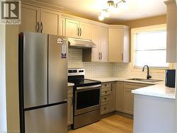 Kitchen featuring light-toned cabinetry with dark hardware, stainless steel appliances, a white subway tile backsplash, and light wood-finish flooring - 