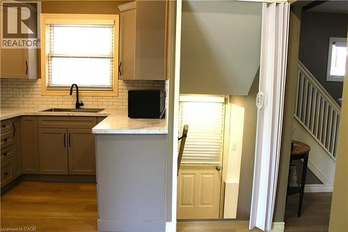 Kitchen featuring wood-finish flooring, shaker-style cabinetry, a subway tile backsplash, and light-toned countertops - 4935 Willmott Street, Niagara Falls, ON 