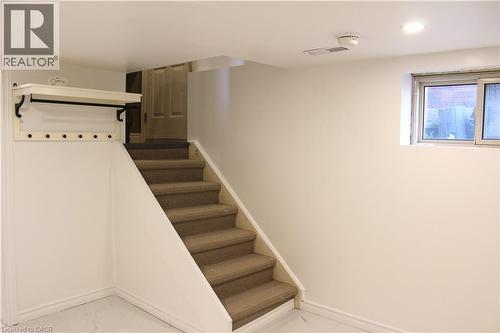 Carpeted staircase with white risers and a built-in wall shelf featuring a coat rack - 4935 Willmott Street, Niagara Falls, ON 