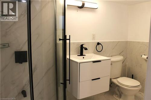 Bathroom featuring a glass-enclosed shower with matte black hardware, a wall-mounted vanity with integrated sink and storage, a matte black faucet, and white tile flooring with veining - 4935 Willmott Street, Niagara Falls, ON 