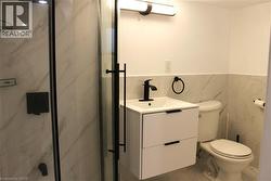 Bathroom featuring a glass-enclosed shower with matte black hardware, a wall-mounted vanity with integrated sink and storage, a matte black faucet, and white tile flooring with veining - 