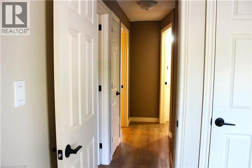 Hallway featuring wood-finish flooring, white paneled doors with matte black hardware, and neutral wall paint - 4935 Willmott Street, Niagara Falls, ON 