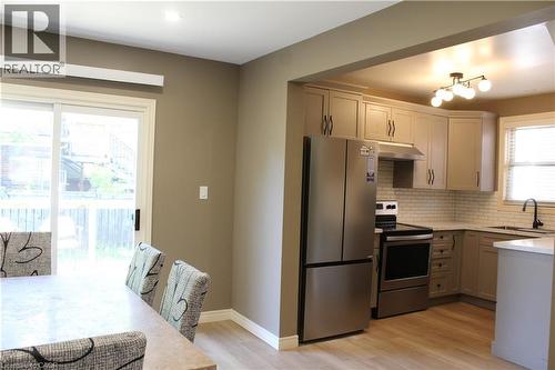 Kitchen featuring stainless steel appliances, light wood-finish flooring, white subway tile backsplash, light grey cabinetry, and a black-finish faucet - 4935 Willmott Street, Niagara Falls, ON 