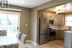 Kitchen featuring stainless steel appliances, light wood-finish flooring, white subway tile backsplash, light grey cabinetry, and a black-finish faucet - 