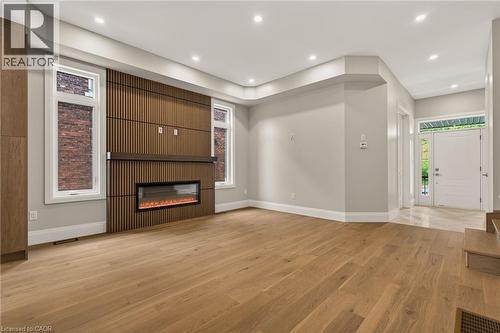 Spacious room featuring wood-finish flooring, a contemporary fireplace with a slatted wood-finish accent wall, recessed lighting, and a white entry door with frosted glass detailing - 279 Hess Street S, Hamilton, ON - Indoor With Fireplace