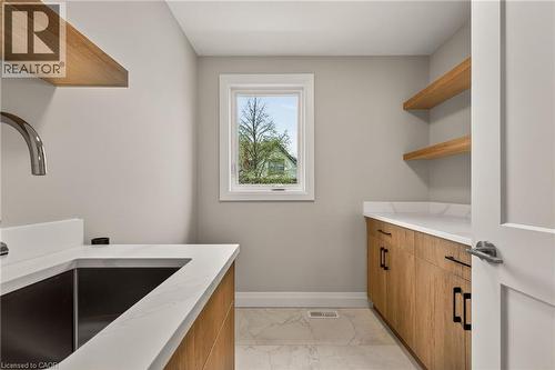 Laundry room featuring wood-finish cabinetry, white countertops, a stainless steel sink with a gooseneck faucet, and open wood-finish shelving - 279 Hess Street S, Hamilton, ON - Indoor Photo Showing Other Room