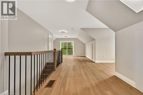 Hardwood flooring extending throughout an open loft area with a contemporary black metal and wood-finish railing - 279 Hess Street S, Hamilton, ON - Indoor Photo Showing Other Room