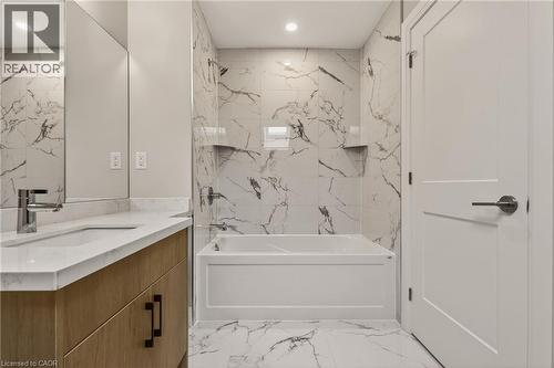 Bathroom featuring a wood-finish vanity with a white countertop and undermount sink, a large mirror, a tiled tub/shower combination with recessed shelving, and a matching tiled floor - 279 Hess Street S, Hamilton, ON - Indoor