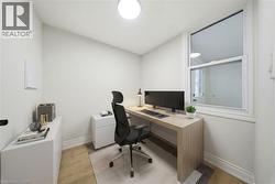 Dedicated office space featuring a large window, light wood-finish flooring, white walls, and a round overhead light fixture Virtually Staged - 