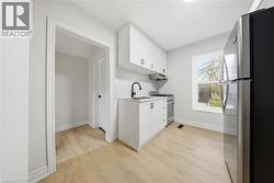 Kitchen featuring white cabinetry, light wood-finish flooring, a stainless steel refrigerator, and a black faucet - 