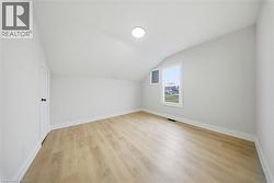 Bright room featuring a sloped ceiling, wood-finish flooring, white baseboards, and a single window - 