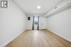 Spacious room featuring light wood-finish flooring, white baseboards, and a white ceiling with recessed lighting - 