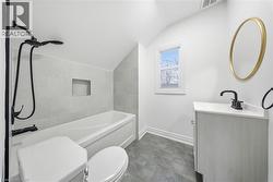 Bathroom featuring a white bathtub with a tiled surround, a built-in shower niche, and a matte black shower fixture - 
