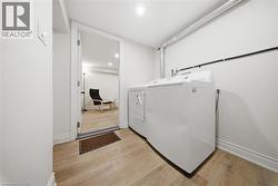 Dedicated laundry area featuring a white top-load washing machine and dryer, wood-finish flooring, and crisp white walls - 