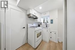 Compact kitchen featuring white cabinetry, a gas range with range hood, a stainless steel sink with a matte black faucet, and wood-finish flooring - 