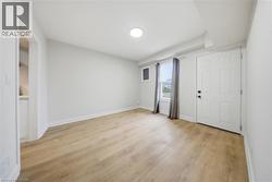 Spacious room featuring light wood-finish flooring, white walls, a recessed ceiling light, and a white paneled door - 