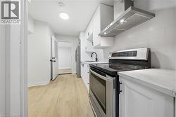 Bright kitchen featuring wood-finish flooring, white cabinetry, a stainless steel range with overhead ventilation, and a black faucet - 
