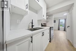Kitchen featuring white shaker-style cabinetry with matte black hardware, double stainless steel sink with matte black faucet, and white subway tile backsplash - 