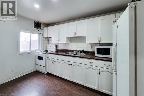 Kitchen featuring white cabinetry, dark countertop, double basin sink, and wood-finish flooring - 463 Wellington Street N, Hamilton, ON - Indoor Photo Showing Kitchen With Double Sink