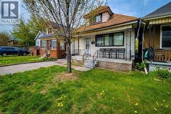 Single-family residence featuring a front porch with metal railings, a dormer window, and a paved driveway leading to a rear parking area - 