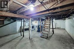 Unfinished basement featuring a utility sink, laundry hookups, exposed wooden ceiling joists, and a partial staircase - 